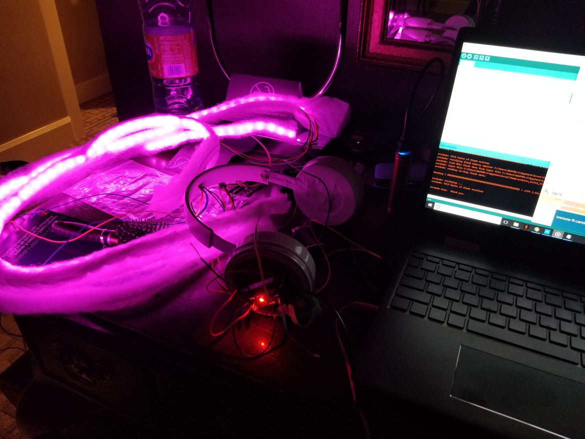 a wig fitted with pink LEDs lies next to a laptop and an assortment of electronics